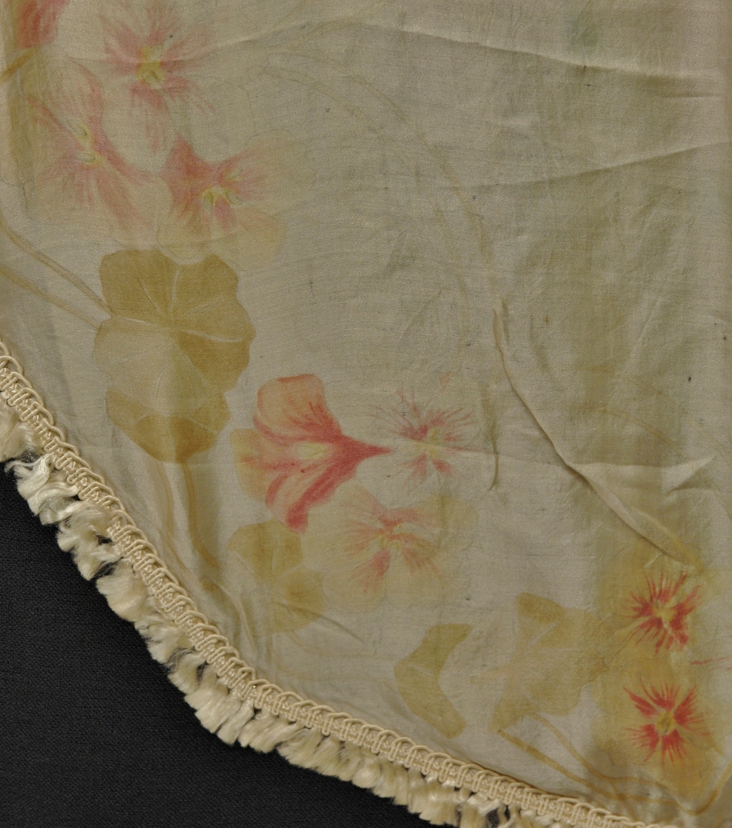 Rund duk i silke med påsydd frynsekant. Påtrykket rosemønsteri rosa og grøn på gul bunn.