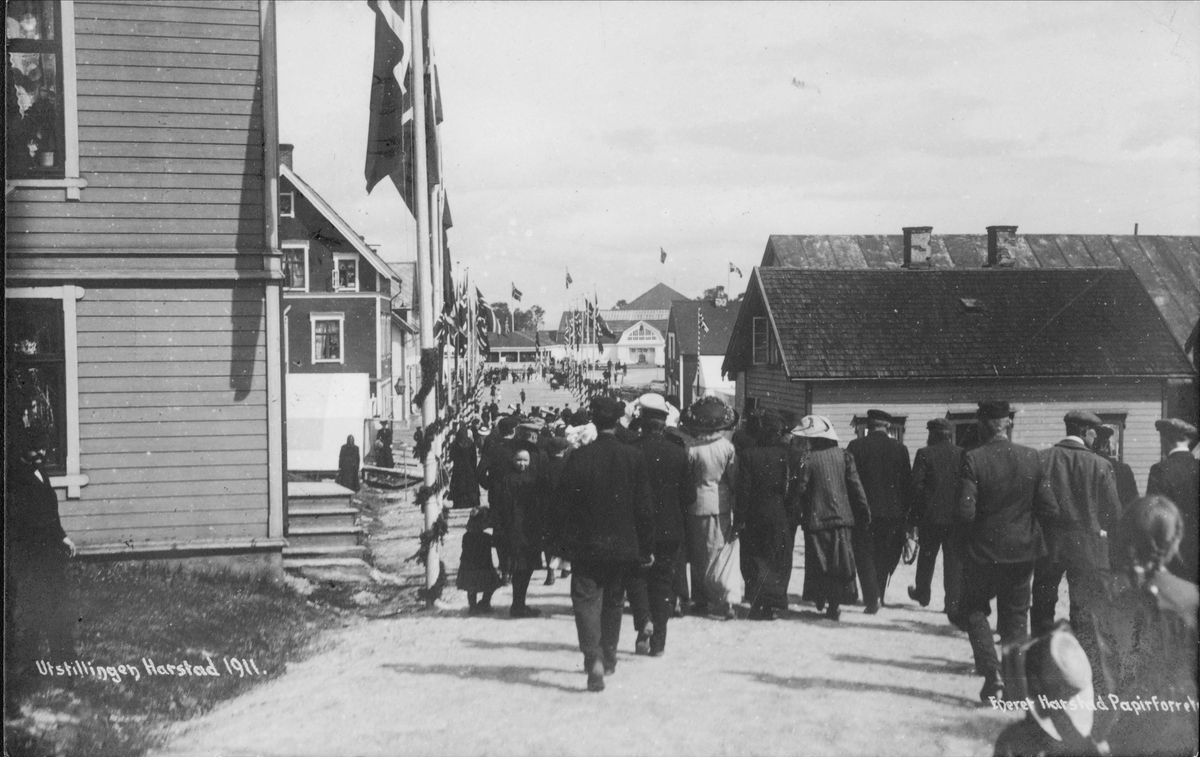 Mennesker på tur ned Havnegata. Utstillingspaviljongen på Hamnneset i bakgrunnen, Klæboegården i forgrunnen til venstre, Isaksengården til høyre.