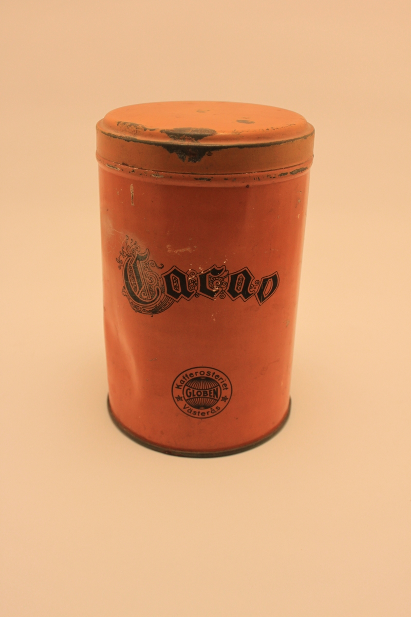 Cylinderformad orange plåtburk med lock för kakao. Med svart text "Cacao".