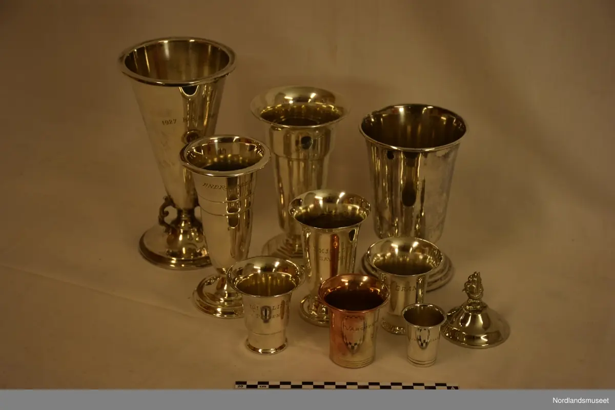 Ni sølv pokaler, en stor grønn banne, to blå liten trekantet flagge, to  runde keramik og diverse tekster om klubben.