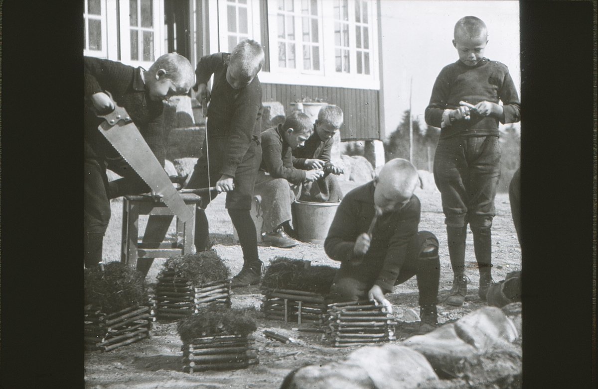 Gutter på friluftsskolen Vangen bygger en bondegård i miniatyr. To gutter sitter i bakgrunnen og skreller poteter.