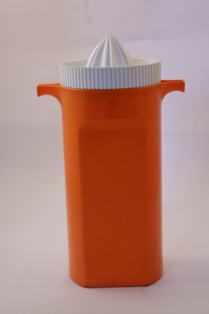 Kombinerad tillbringare och citruspress i plast.  Locket i vit plast är formad som en citruspress. Tillbringaren i orange plast har två pipar en på var sida högst upp på tillbringaren.