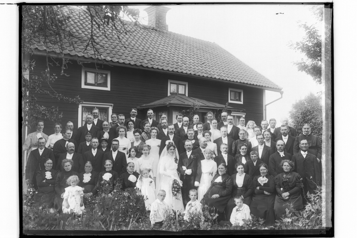 Bröllop, brudpar och bröllopsgäster.
Bostadshus i bakgrunden.
Karl Johan Andersson