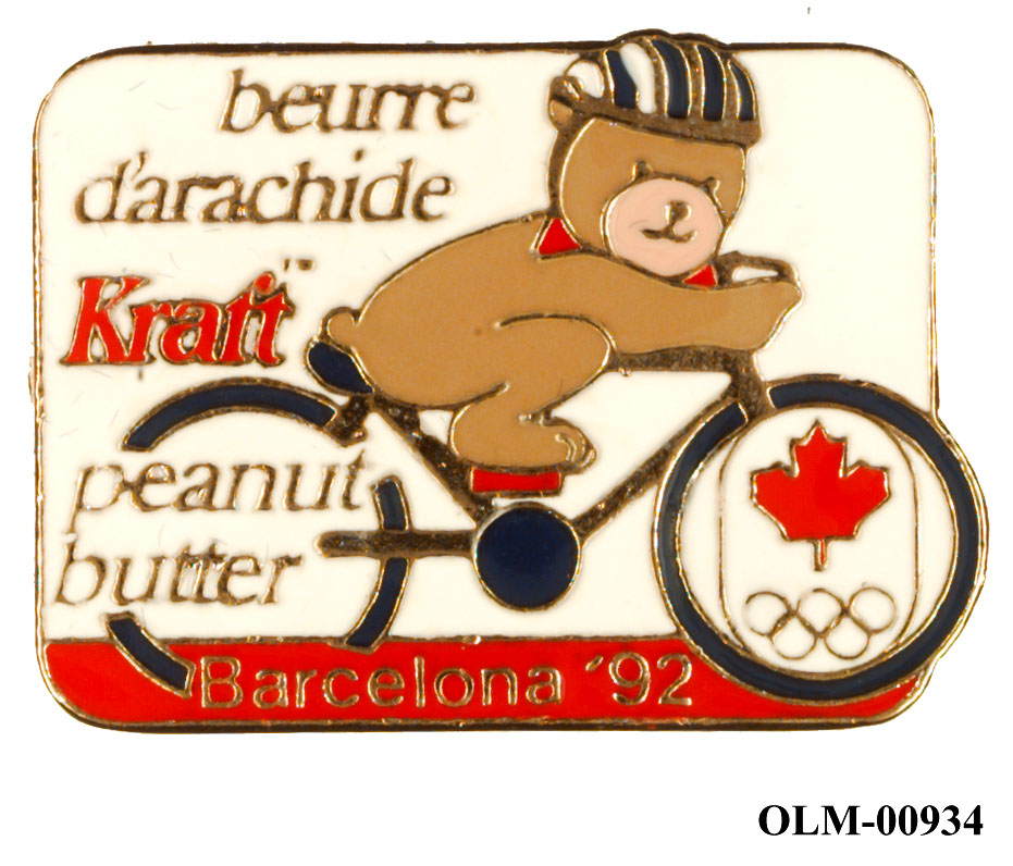 Liggende rektangulært merke med bilde av en bjørn på sykkel med hjelm. Canadas lønneblad i rødt i forhjul nederst til høyre og tekst til venstre.