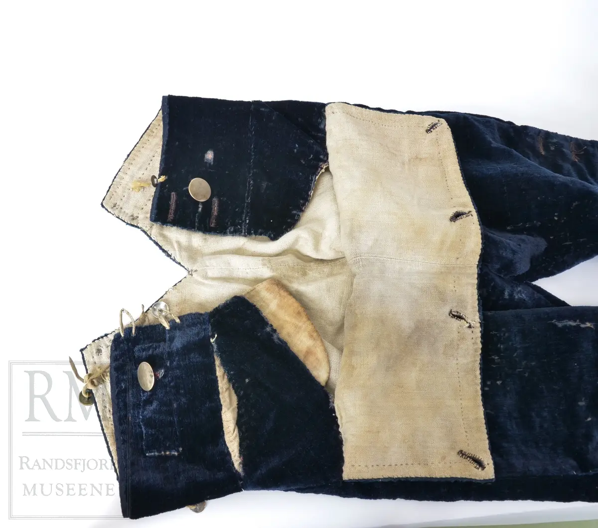 Mørk blå fløyelsbukse, knelang, med lem. Foret i lin. Fem flate messingknapper.