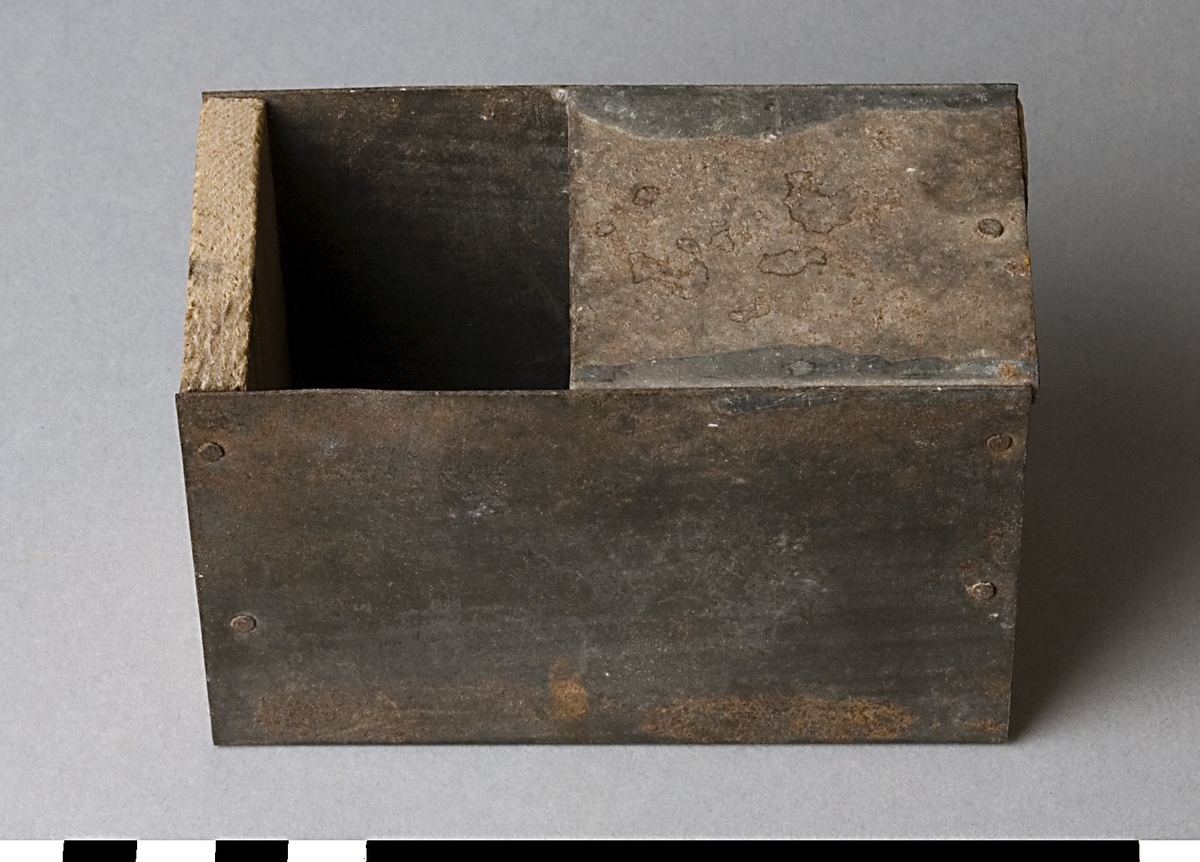 Låda, troligen för förvaring av spik eller liknande. Lådan är tillverkad av plåt med botten och överdel av trä. Övre halvan av framsidan är öppen.