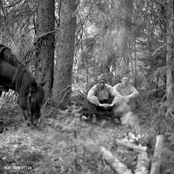 Kaffevarme i granskog.  Ved bålet satt det to unge menn på e