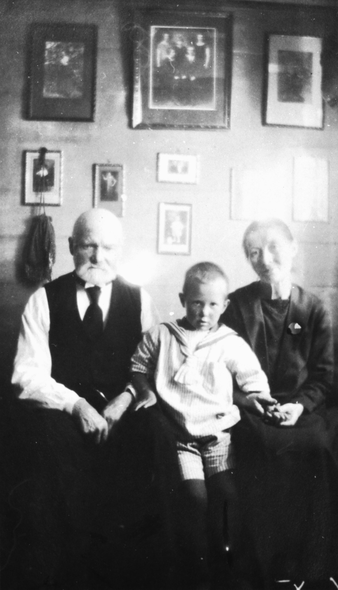 Portrettfotografi av Arnt og Marta Ystenes m/ sønn. Fotografert i stuen til Dybhuset på Buholmen. Dette huset er senere flyttet til Sunnmøre Museum.