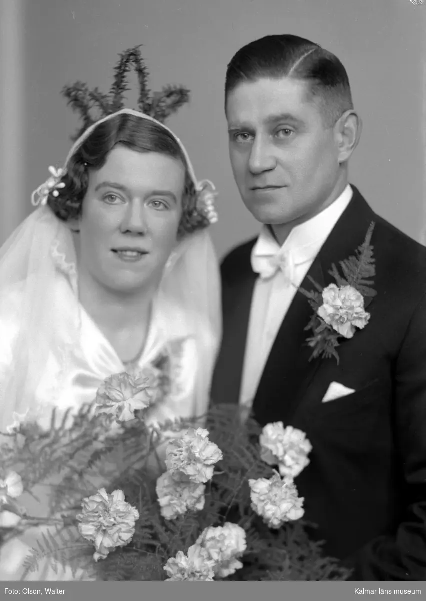 Ateljébild på ett brudpar. Kvinnan har brudklänning och myrtenkrona. Enligt Walter Olsons journal är bilden beställd av Emil Carlsson.
