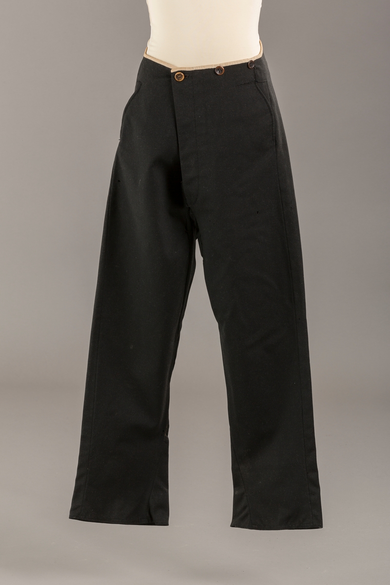 Form: Bena utvidet nederst. Lerretskant rundt livet, spensel i ryggen, mangler spenne i sepnsel?
Delvis foret. To lommer. 5 knapper, mangler en knapp.