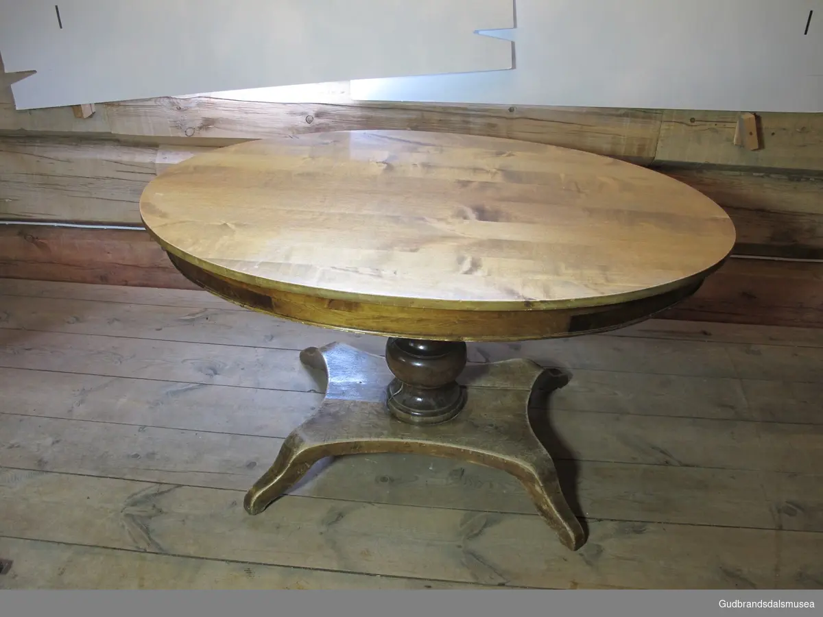 Salongbord, et biedermeierbord. Bordet har oval bordplate over en kraftig dreid stod. Underst er det en mindre plate med fire små bein. Bordet er lakket.