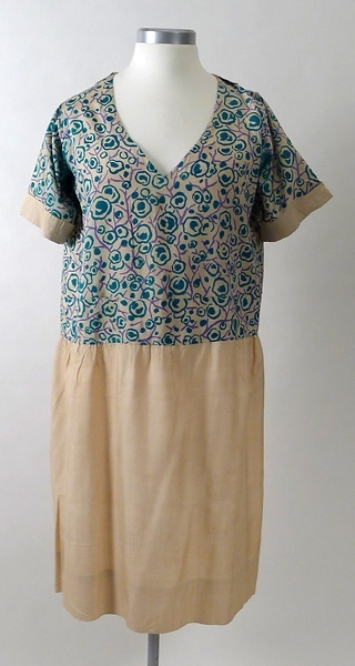Klänning av chantung. Kjolen är sydd av ofärgad chantung. Överdelen i chantung har ett tryckt mönster i grönt och lila. Framtill på livet finns två fickor. Krage baktill. 1920-talet.