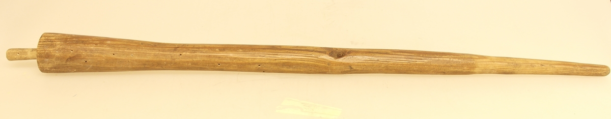 Rund trepinne i skåret furu. Pinnen smalner av i den ene enden. I den tykkeste enden er det en tapp. Det er et hull midt i pinnen.