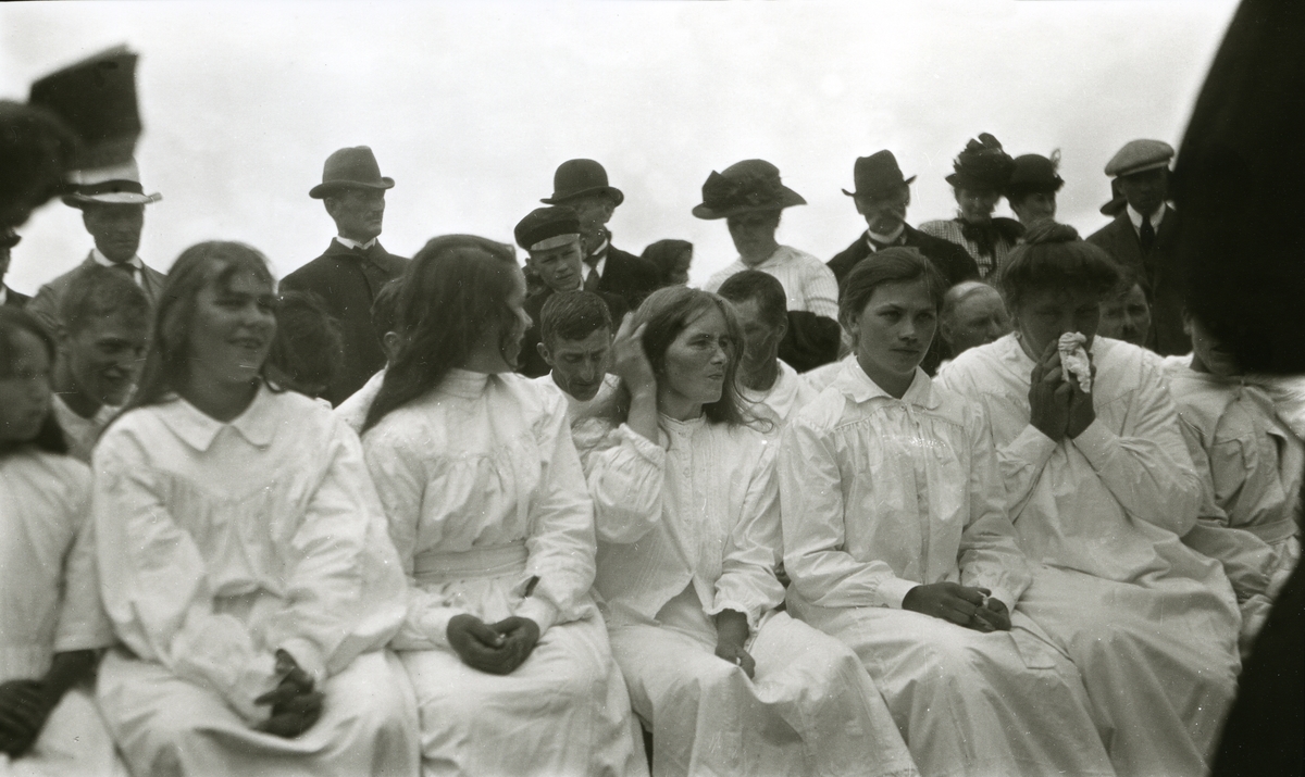 Menn og kvinner i hvite kjoler, sittende, venter på å bli døpt i Älvdalens finnmark, Sverige.