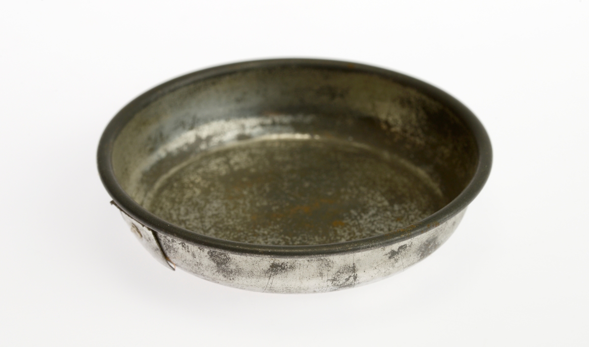 En liten komfyr med tre kasseroller og en steikepanne. Gjenstandene er undernummerert 01-05.
FTT.54454.01: En svartlakkert lekekomfyr som er firkantet med avrundede hjørner. Den er trolig laget av jernblikk og blikk. På kokeflaten er det tre hull for å plassere kasserollene på. Bakerst til venstre er det en 8cm høy pipe. I front er det en sølvfarget blikkdør som er festet med hengsler. På døren er det innskrift og et lite messingfarget og rundt håndtak. Komfyren har buede bein.
FTT.54454.02: En høy kasserolle laget av blikk. I hver side er det loddet på håndtak. 
FTT.54454.03: En lav kasserolle laget av blikk. I hver side er det loddet på håndtak.
FTT.54454.04: En lav kasserolle laget av blikk. Det har vært festet et langt håndtak i den ene siden, men det er nå løs.
FTT.54454.05: En steikepanne laget aav blikk. Håndtaket mangler.