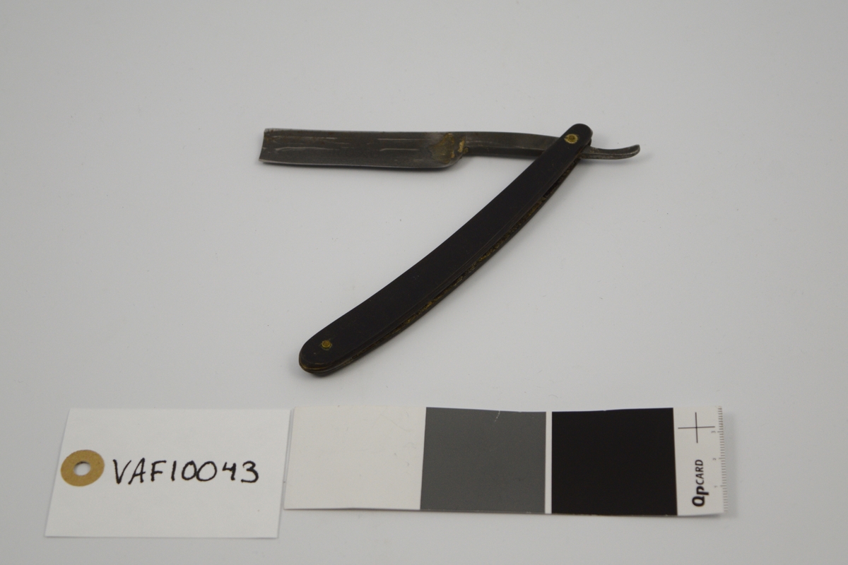 Sammenleggbar barberkniv med rett egg. Knivbladet har konisk tverrsnitt. Bladet munner ut i tynt skaft
med en krumning som holdegrep med fingeren. Skaftet er naglet fast til
kniven. Består av to deler som fungerer som beskyttelse i sammenlagt
stilling.