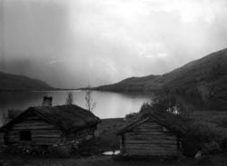 Landskapbilde, med to tømmerhus i forgrunnen. Datering usikk