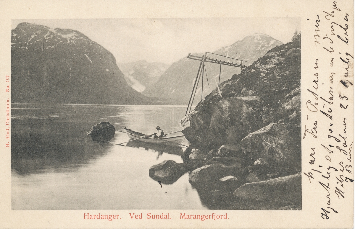 Postkort m/mann i båt ved land. Heiseinnretning. Blikkstille fjord. Hardanger. Sunndal. Marangerfjord. Hilsen til fru Pedersen.