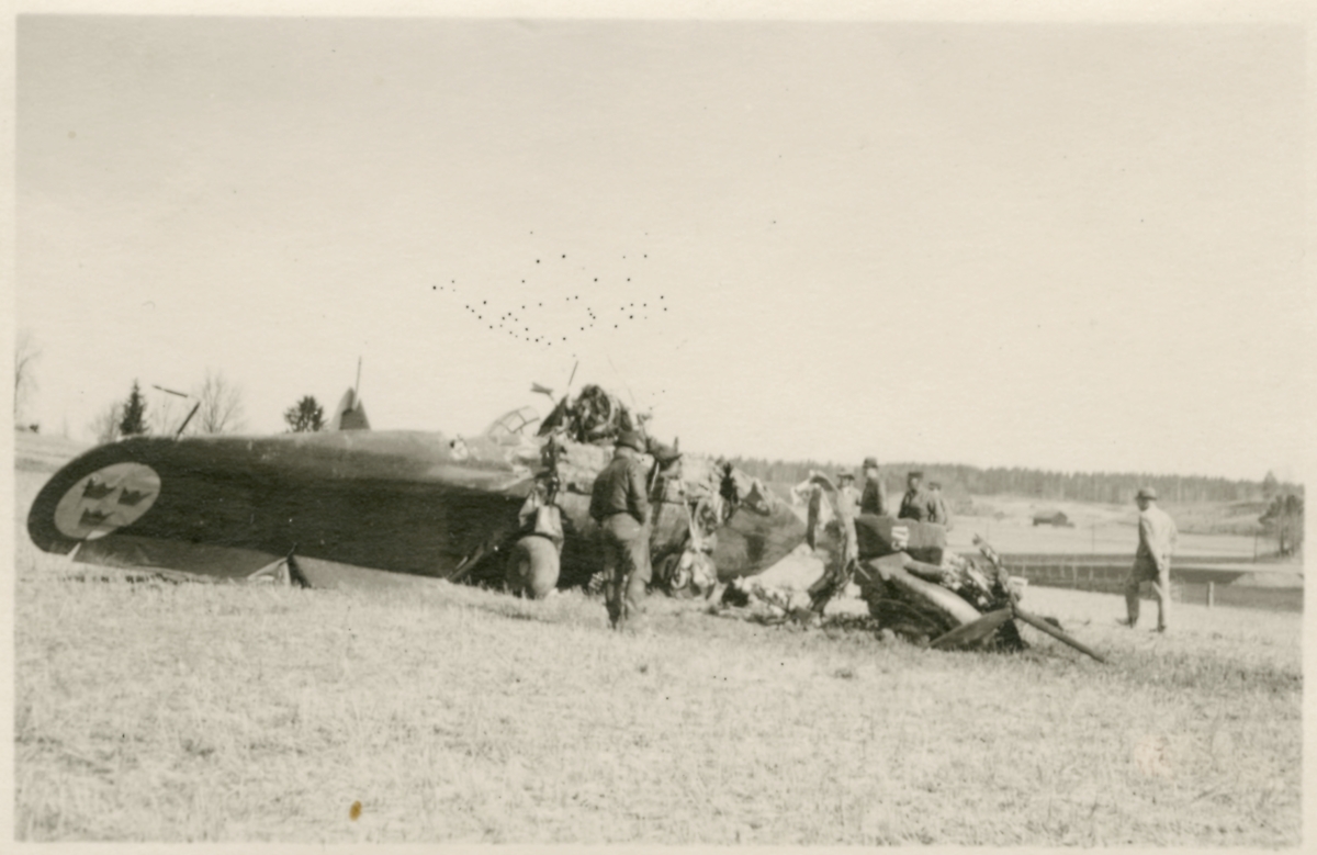 Havererat militärt skolflygplan SK 14 nummer 675, märkt F 5-175 på ett fält utanför Vittsäter, sydost om Nykil i Östergötland, den 30 april 1940. Män i närheten av flygplanet. Serie om 8 bilder.