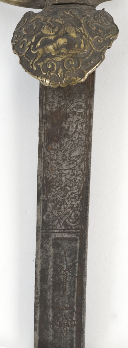 Knapp i form av hvelvet hette med dyreornamentikk og nedbøyd skjell på utsiden. Tregrep belagt med skilpaddeskall. Fremre parerstang går over i håndbøylen. Bakre parerstang ender i et stilisert dyrehode.  Nedbøyd skjell dekorert med dyremotiver på utsiden.
Enegget klieformet klingen med ryggslipning mot spissen. Klingen har en bred og en smal ryggstillt blodrand. Klingen har etset rankedekor på begge sider.
Lærbalg sydd på innsiden med messingbånd på toppen.