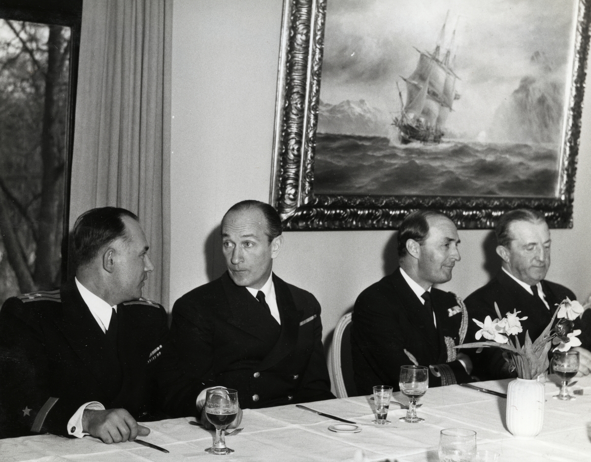 Konteramiral Samuelson (till höger) och kommendörkapten Linde af Hageby (andra från vänster) tillsammans med två andra militärer sitter på rad vid ett dukat matbord. Samtliga är klädda i uniform.