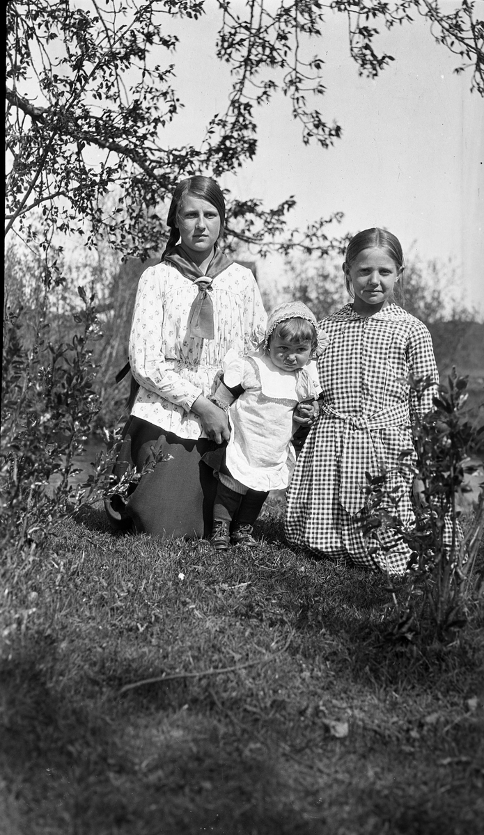 Tre jenter, den ene et barn, på kne i hagelignende omgivelser. Småjenta i midten er Nora Gunnerød, til høyre Asta Lovise Gunnerød. Jenta til venstre kan muligens være Aslaug Gunnerød, men dette er usikkert.