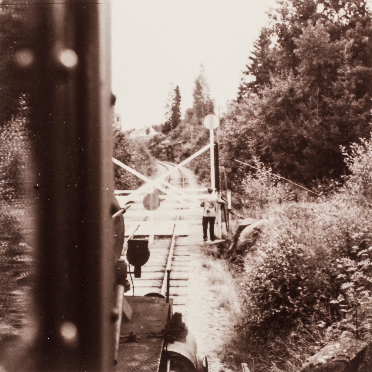 På Vestmarkalinjen måtte togpersonalet selv betjene planovergangene og åpne og lukke grindene. I bakgrunnen tog med fullastede plankevogner underveis til Skotterud. Fotografert fra lokomotivet, damplok type 21.