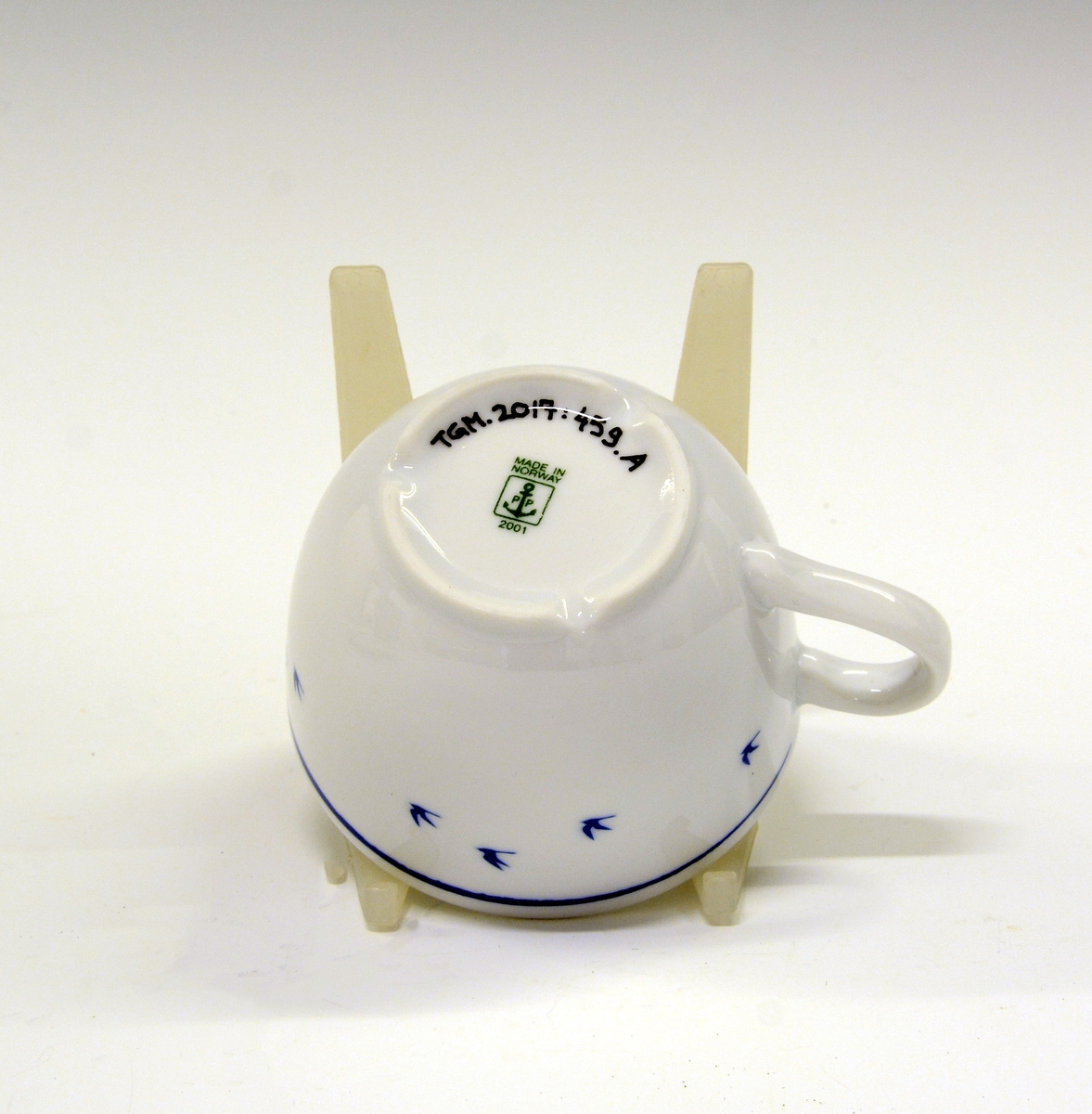 Kopp av porselen med hvit glasur. Dekorert med blå strek og blå flyvende fuglesilhuetter.
Modell: Roma