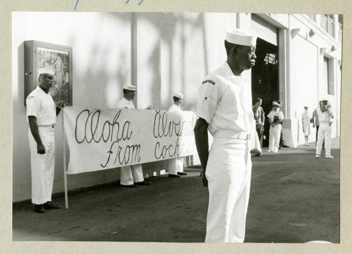Bilden föreställer män i vita uniformer som står tillsammans med en välkomstskylt med text på. Bilden är tagen under minfartyget Älvsnabbens långresa 1966-1967.