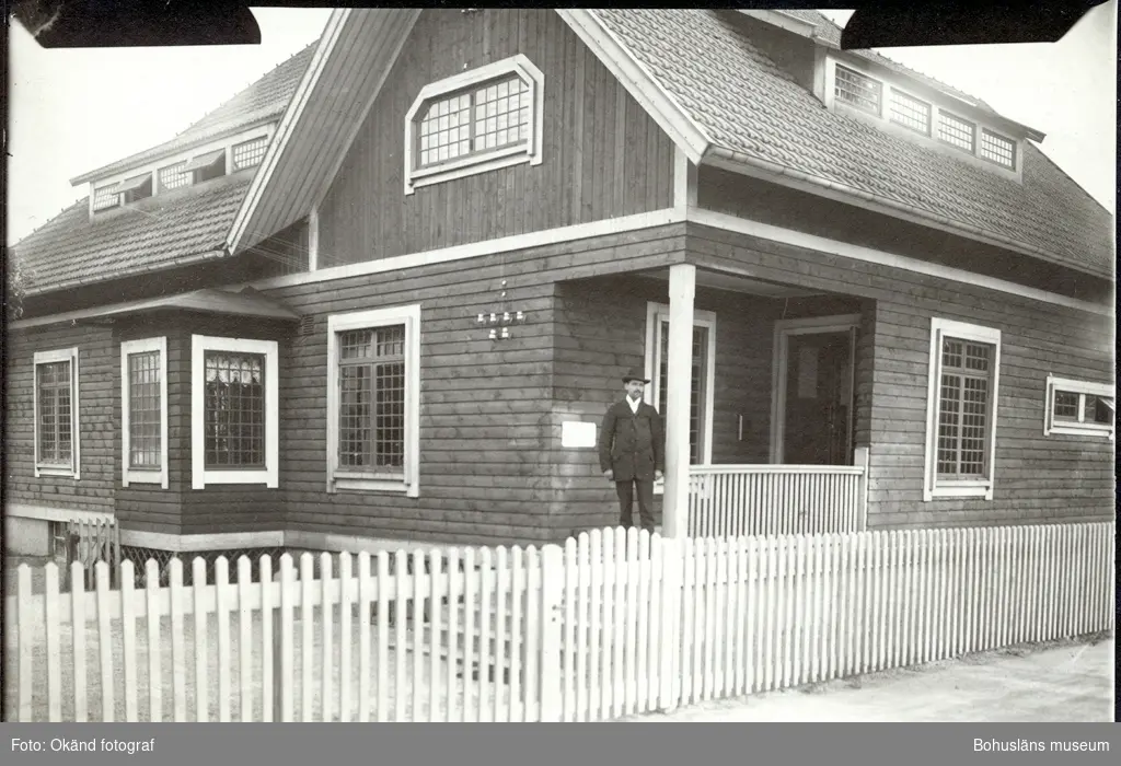 En man står på en veranda på ett stort hus med staket runt om