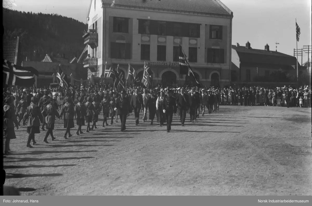 17. mai feiring 1931. Folketog på Notodden torg. Poitimenn og speidere med flagg i front av barnetoget. Notodden apotek i bakgrunnen.