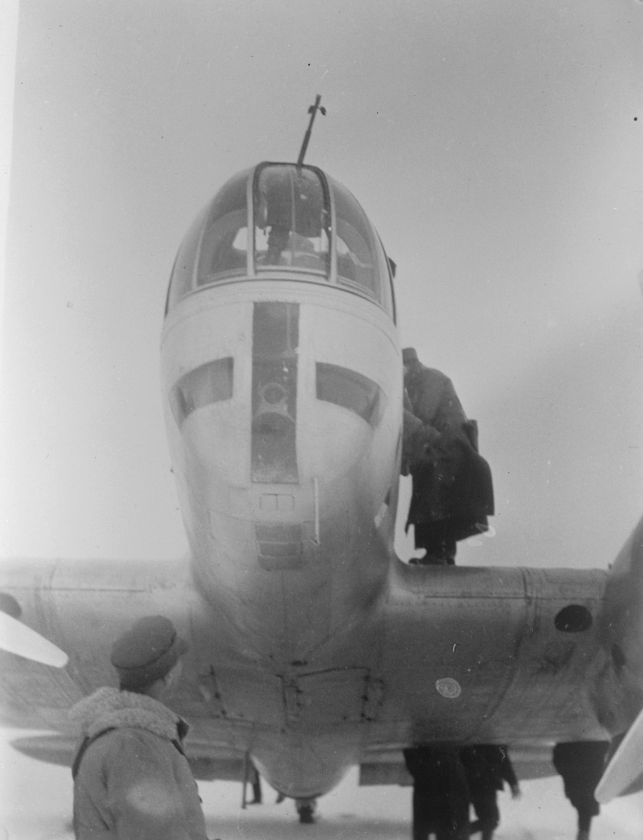 Närbild av nos av sovjetiskt flygplan Iljushin DB-3 på ett fält under finska vinterkriget, 1940. Människor i rörelse runtomkring. Bild från F 19, Svenska frivilligkåren i Finland.