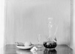 Stilleben, karaffel, glass og fruktfat med frukt.