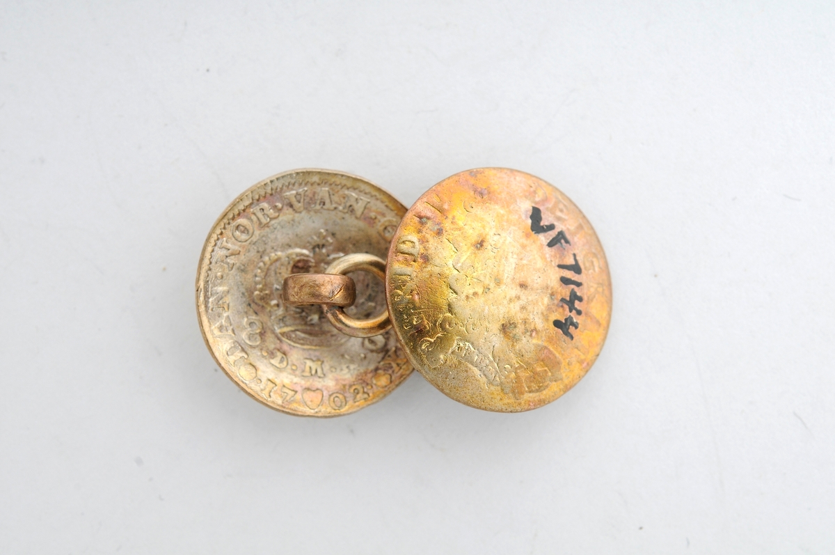 Sølje, halsknapp i sølv. Sett saman av to knappar i ei åttetallsforma hempe i messing. Knappane er gamle myntar frå 1702 og 1704, og som er laga om til knappar. (sjå nærmare registrering på arkivkort 7144).