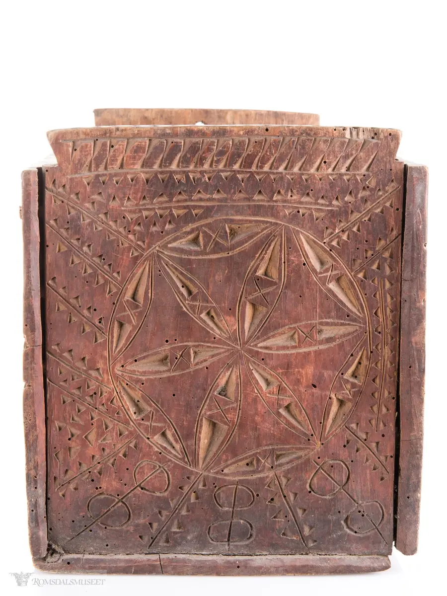 En stor og to små seksbladsroser i karveskurd på langsidene med skraverte dekorfelter og spetter rundt. På kortsidene er det skåret ut en stor seksbladsroser med rike dekorasjonsfelter bestående av spetter, streker diamantformer, sirkler med strek gjennom og solkors/kors. De største rosenen har kryss skåret inn på kronbladene.