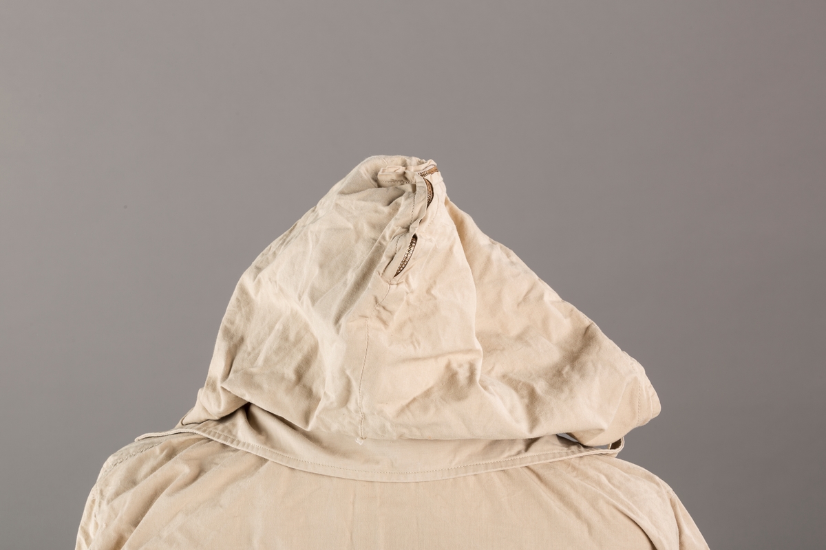 Form: Vanlig anorakkfasong med strikk i livet. 2 brystlommer med knapp.
Hette med glidelås på topp midt, snøring.
Glidelås helt ned foran.
Innermansjett med strikk i ermene.