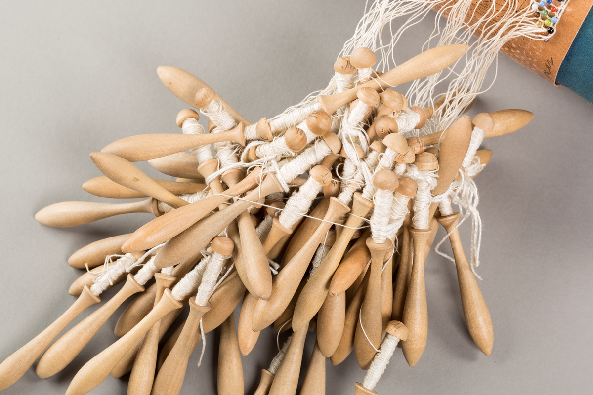 Form: Sylinderformet "pute" hvor stivt pappstykke rundt puta viser mønsteret. 
Kniplingsstykke under arbeid påspent med knappenåler
Pinner medkniplingstråd