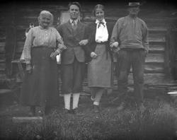 Et eldre og et yngre par står arm i arm ved setervegg.