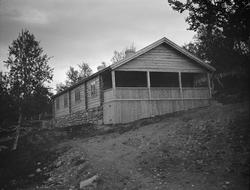 Tømret hytte med veranda på kortsiden som ligger på fjellet.