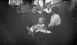 Gruppe barn og voksne sitter i gresset med minstebarnet nake