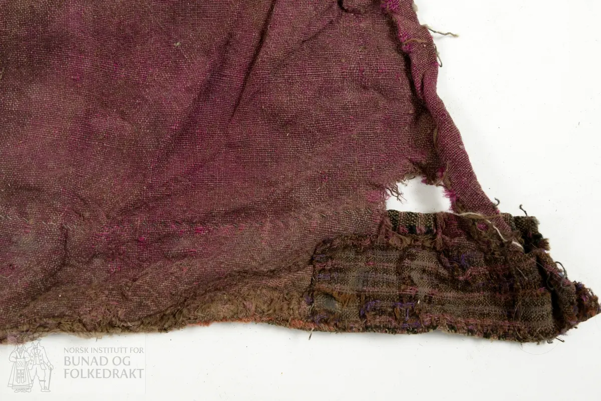 Del av ein stakk, full høgde utan linning. To høgder av brun og lilla verken, lerretsbinding med ull i innslag og renning, sauma saman for hand. Stoppa med eit stort stykke midt på høgda og to gonger i nedkant, truleg med sama stoff som stakken, bortsett frå eine bota i nedkant som er eit stripete stoff i raud, svart og brunt. Framstår som utslitt i fargen med fleire hol etter mus, har vore nytta som stappefille.