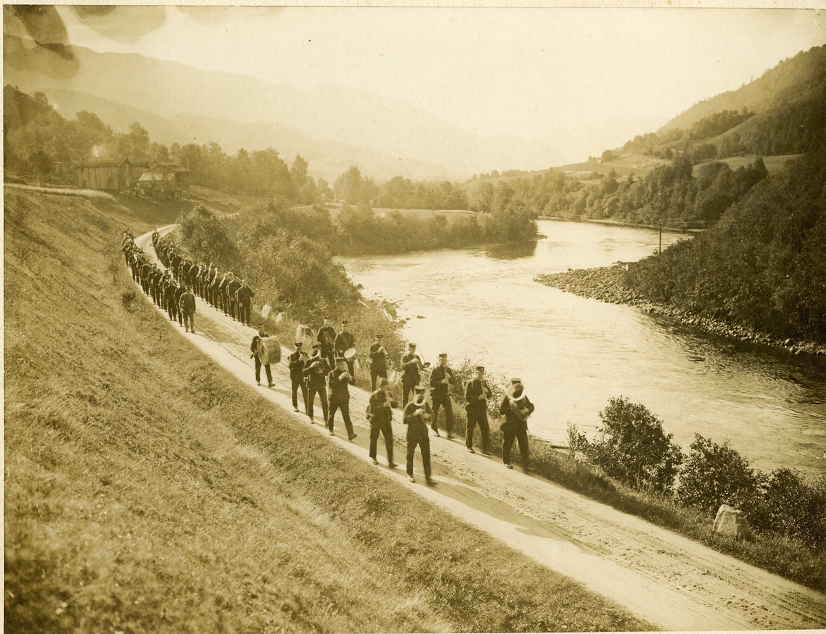 Gruppebilde av divisjonsmusikken på utmarsj nær en elv i Rennebu 1919.