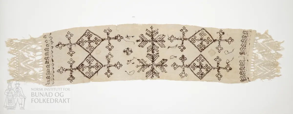 Er usikker på bruken av tekstilen. Kan ha vore sendingsplagg, hovudklut eller bårekross?
Av grov mjuk ubleika linlerret. Jare i båe langsidene. Broderi med holbeinsting med sauebrunt ullgarn. Båe endane har påsydd eit stykkje av liknande linkvalitet, der efsingane er knytt i firflettingsteknikk. Initialane MKD og årstalet 1799.