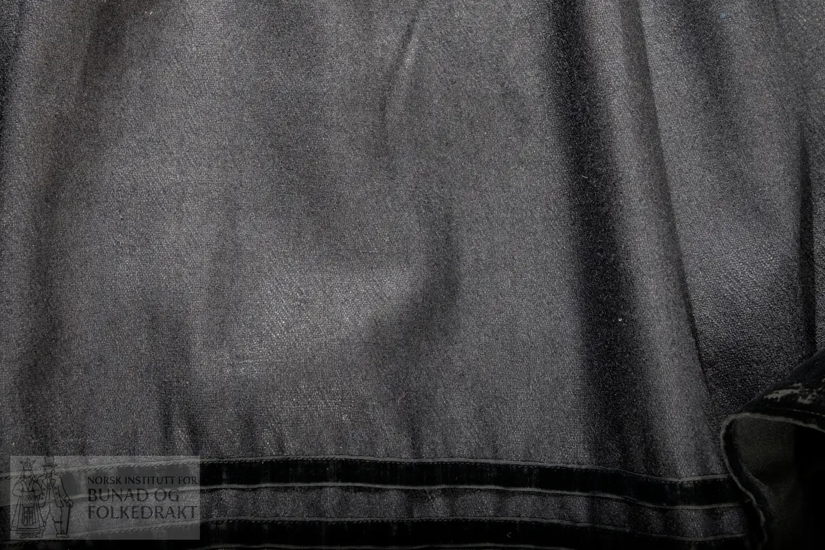 Liv sauma av raud ullkypert, lett valka. Fora med ubleika bomullslerret.
Ermhole, rundt hals og opning framme er kanta med blomstermønstra fleirfarga fløyelsband med svært avslitt fløyel. Innanfor kantingar er det påsett eit smalt metallband.
Etter framkantane er det påsett 3 borer på kvar side, dei to øverste litt breiare enn dei fire nederste, alle har eit skåleforma lauv festa i midten. På framsida av den kurva delen er det fem ulike stempel: 63 i eit sirkelforma stempel, truleg årstalsstempel. Månadsstempel: 6 over M i rektangelforma stempel. Mesterstempel i bølgeforma ramme LAR, Lorentz Christopher Angel Reimers, fekk borgarskap i Bergen i 1832. Lødighetsstempel 13 1/3. Trapesforma stempel med 7 prikkar, Bergens bystempel.
Lukking framme med to metallhekter på kvar side.
Heile livet er sauma på maskin. Kanting er sauma for hand. 
Livet sauma på stakken for hand. 
Stakken er av heimevove ullerret, blåsvart. Splittopning midt framme. Samansett av 5 rette høgder med jare i begge sider, alle høgder. Faldelagt oppe med eit glatt felt framme mot splitt. Høgdene er sauma saman med maskin. 
Nedkant: 3 svarte smale sillkefløyelsband, nedanfor dei eit påsett stoffstykke av svart bomullsfløyel. Dette stoffet er ein hengefald, ikkje sauma fast i nedkant.
Nedkanten er skonna på innsida med eit lerretsvove mohairstoff av mørk grøn farge. Sauma på med maskin. I nedkant av skonninga er det påsett eit blåsvart kosteband sauma på for hand.
Kanten på linninga er av svart bomullssateng. Er bretta dobbelt og sauma på for hand på begge sider