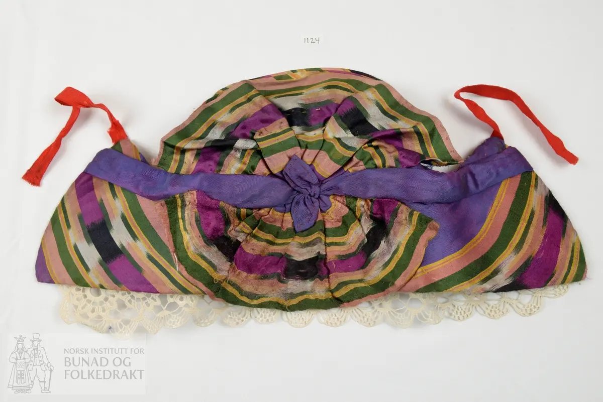 Ei stiv formklipt pappskive trekt med blålilla silketørkle med ikatfarga stripebordar i alle sider. Blårosa kypertvove botn, og fleirfarga striper vove i satengbinding. For av kvit bomullslerret. På innsida av bora er det nåla fast ein hekla blonde - "hetteknipling", hekla av kvitt lingarn og svært stiva. Påsydd knyteband av raud kypertvove ull.