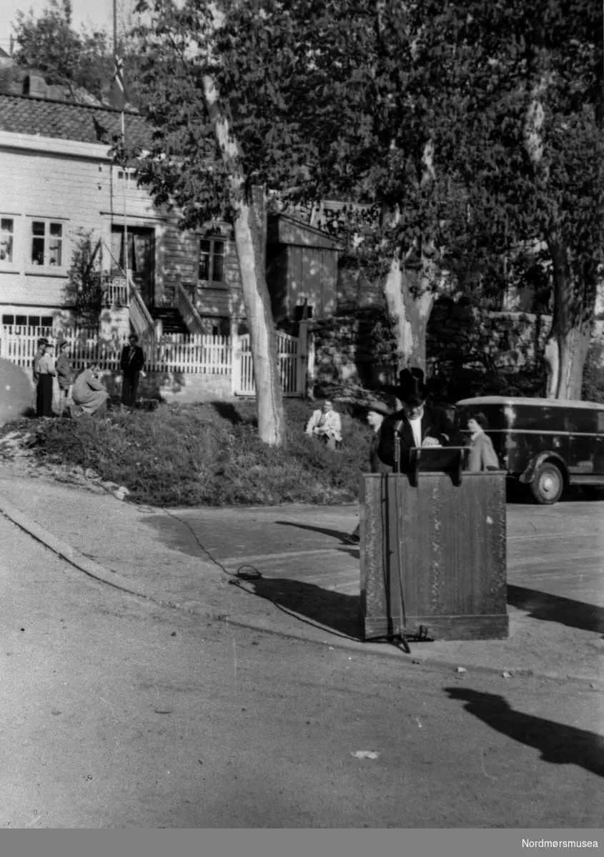 Foto trolig fra en høytidelig tale. Ukjent i hvilken forbindelse. Trolig i Kristiansund. varebil, barn, talerstol på gata. Fra Nordmøre museums fotosamlinger.