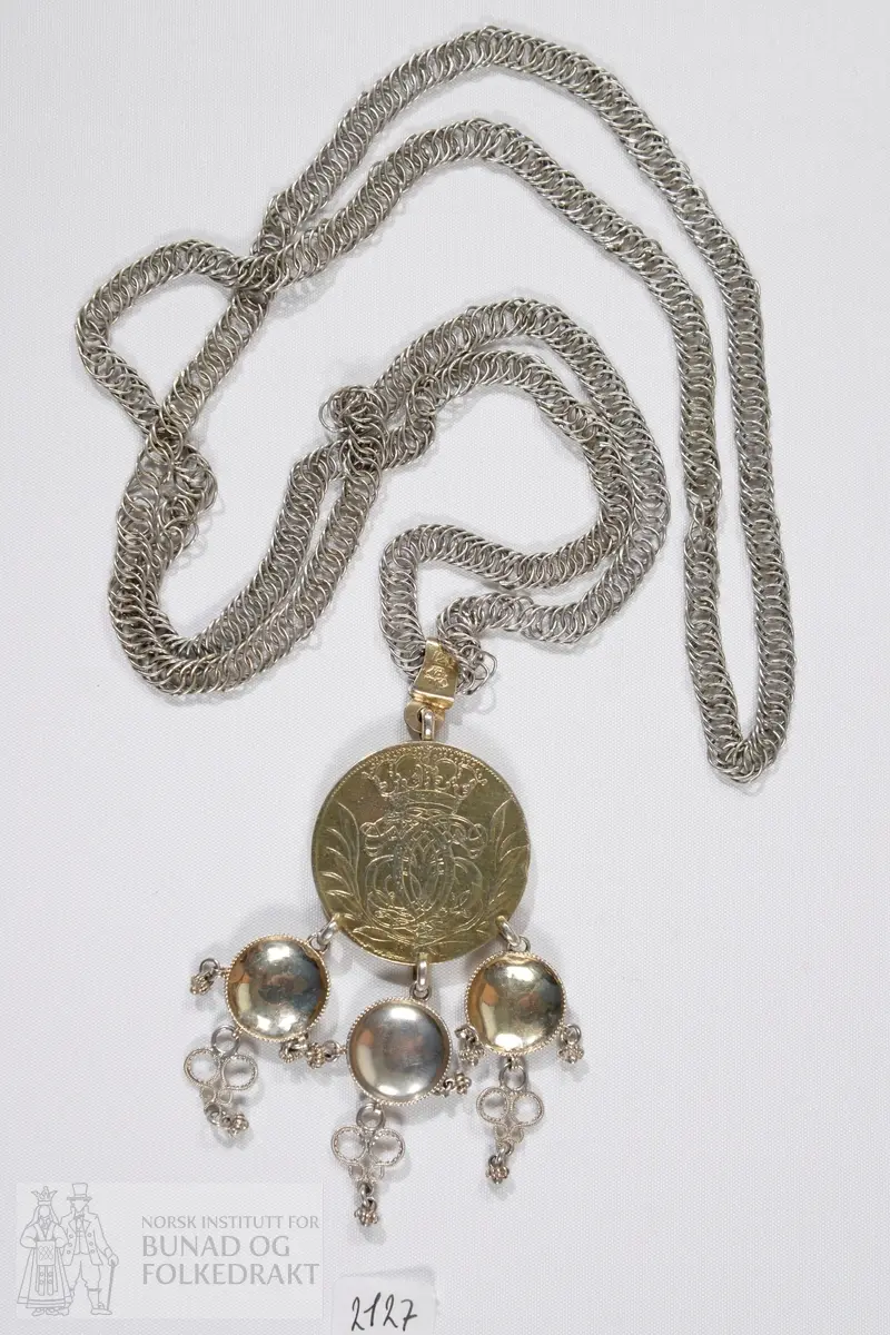 Brudedaler med breikjede. Breikjede er satt sammen av en rekke ringer av sølvtråd festet inn i hverandre. Forgylt mynt med tre ringer påloddet, fra disse henger tre skålformede løv med trådkant, filigranspynt og kruser. Myntens forside: Kronet speilmonogram omgitt av krans. Myntens bakside: Kronet våpen med tre løver, årstallet 1693. Mynten henger i et sølvband på kjedet. På dette bandet er det stemplet: IMS på det ene siden, 12L og gardeinstempel MB 1740.
IMS står for sølvsmed Jacob Michelsen Steen, fra Bergen og med borgerbrev fra 1722. 12L står for 12 lodd, lødigheten i sølvet. De tre skålene er ikke stemplet. 
Mynten er dansk-norsk med Christian den 5.'s speilmonogram, merket 1693.