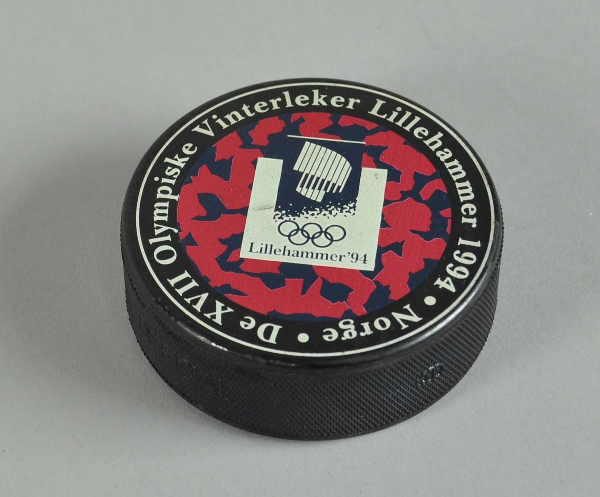 Ishockey-puck med logo for Lillehammer-OL '94 og snøkrystaller i bakgrunnen