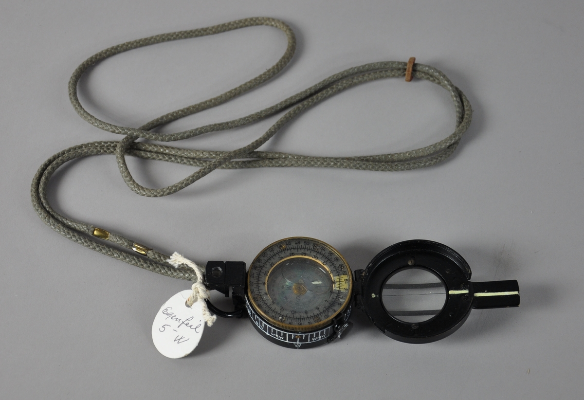 Sort kompass av metall. Til kompasset følger det med en taske av stoff. Tasken har hemper for feste til belte.