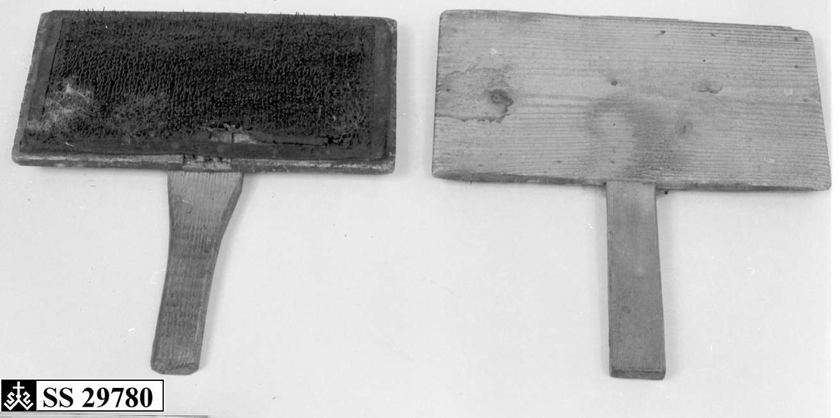 To treplater hvor innsiden av begge platene er dekket av  en skinnduk med tettsittende nåler. Begge treplatene har håndtak.